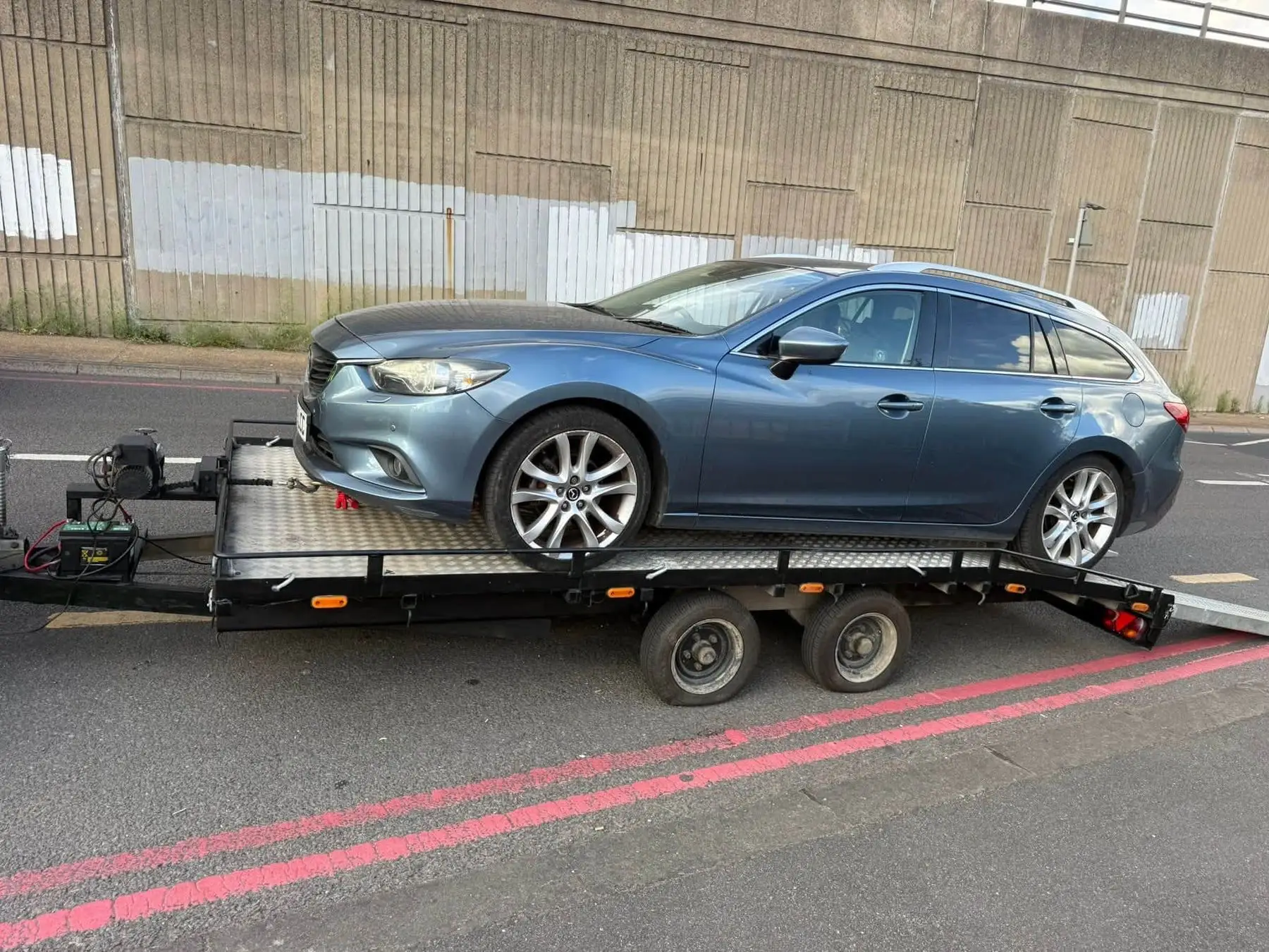 Grey Mazda estate strapped onto the LTR transporter trailer beside a flyover on a London red route