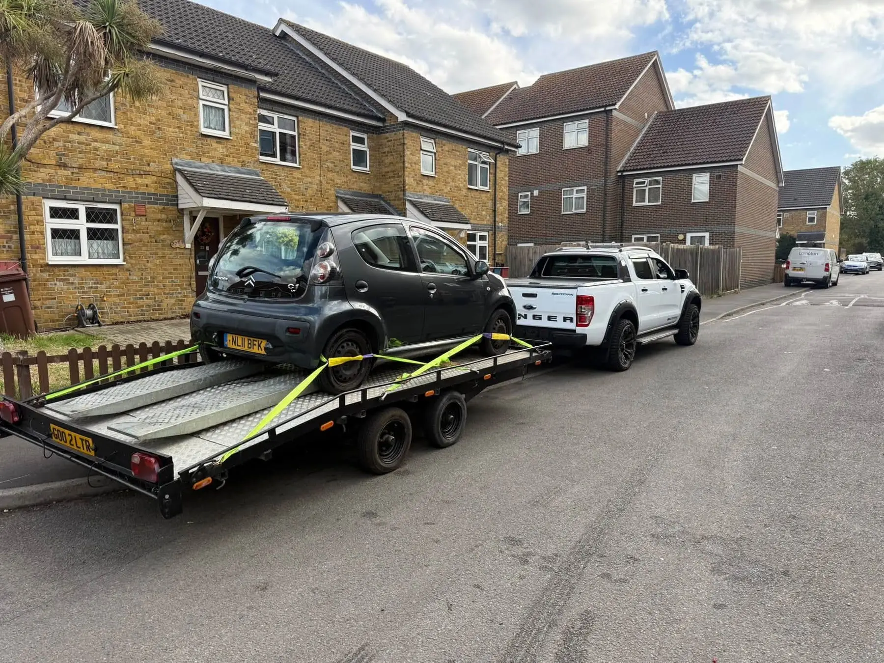 Small city car strapped to the LTR trailer behind the white Ford Ranger on a residential street