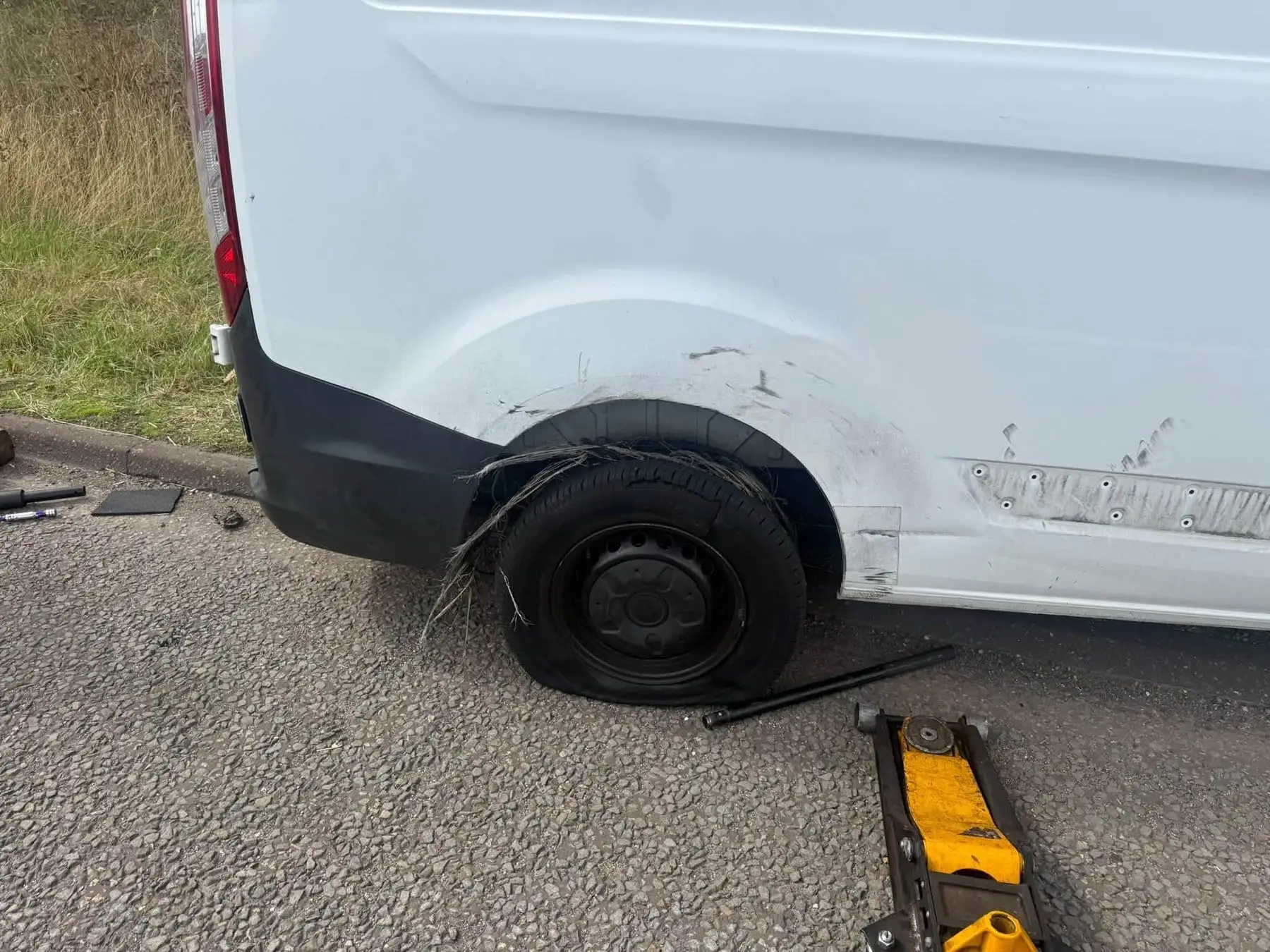 Van with a shredded rear tyre and a trolley jack in position at the roadside